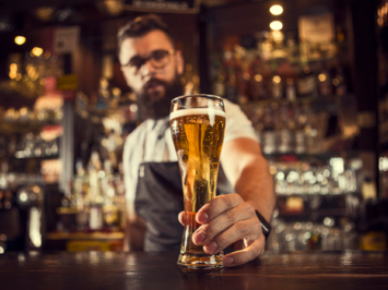 A bartender holds a glass of been on the bar