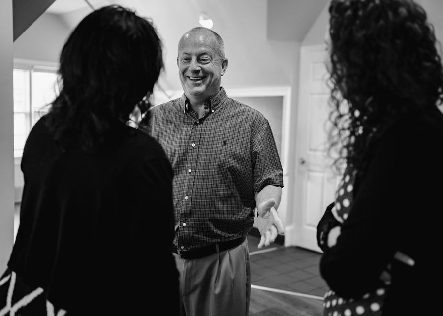A person stand in front of two shadowed individuals with hands out, smiling.